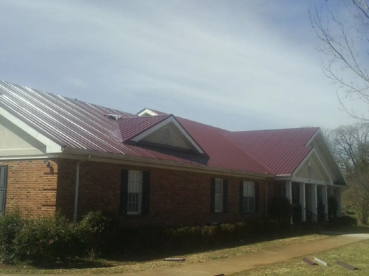 Red metal roof with gabled entries on a long brick building, from a Hail Damage Roof Repair job in Keansburg
