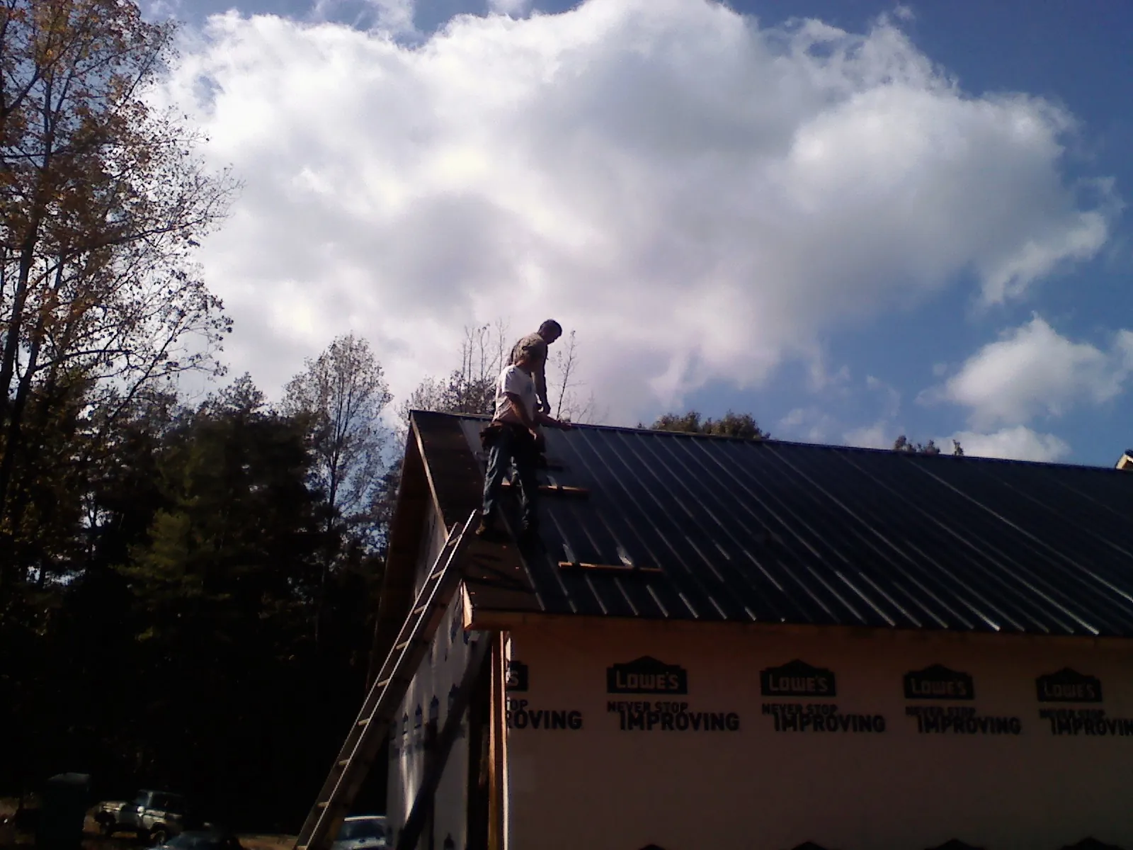 Roofer fastening dark metal panels high against a cloudy sky, from a Roof Inspection job in Keansburg