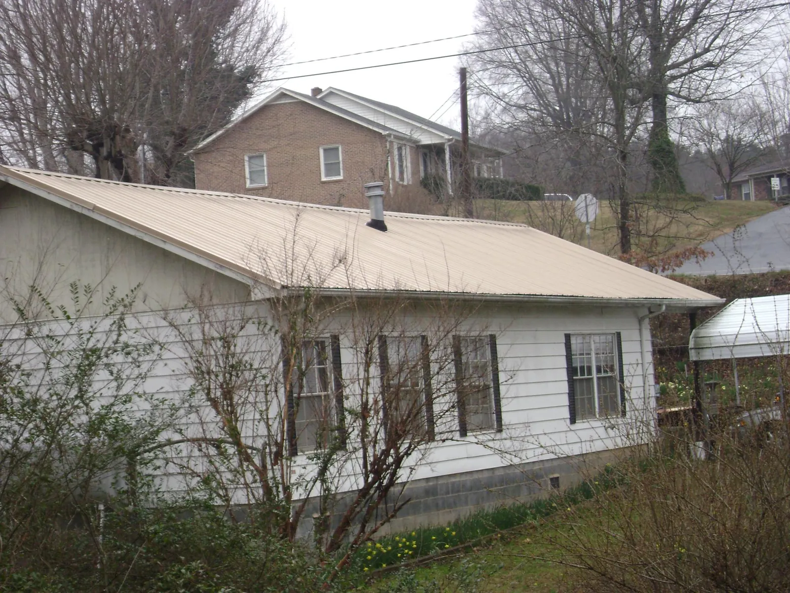 Tan metal roof on a white sided house set into a hillside — Commercial Roofing by Roofing Brothers in Keansburg
