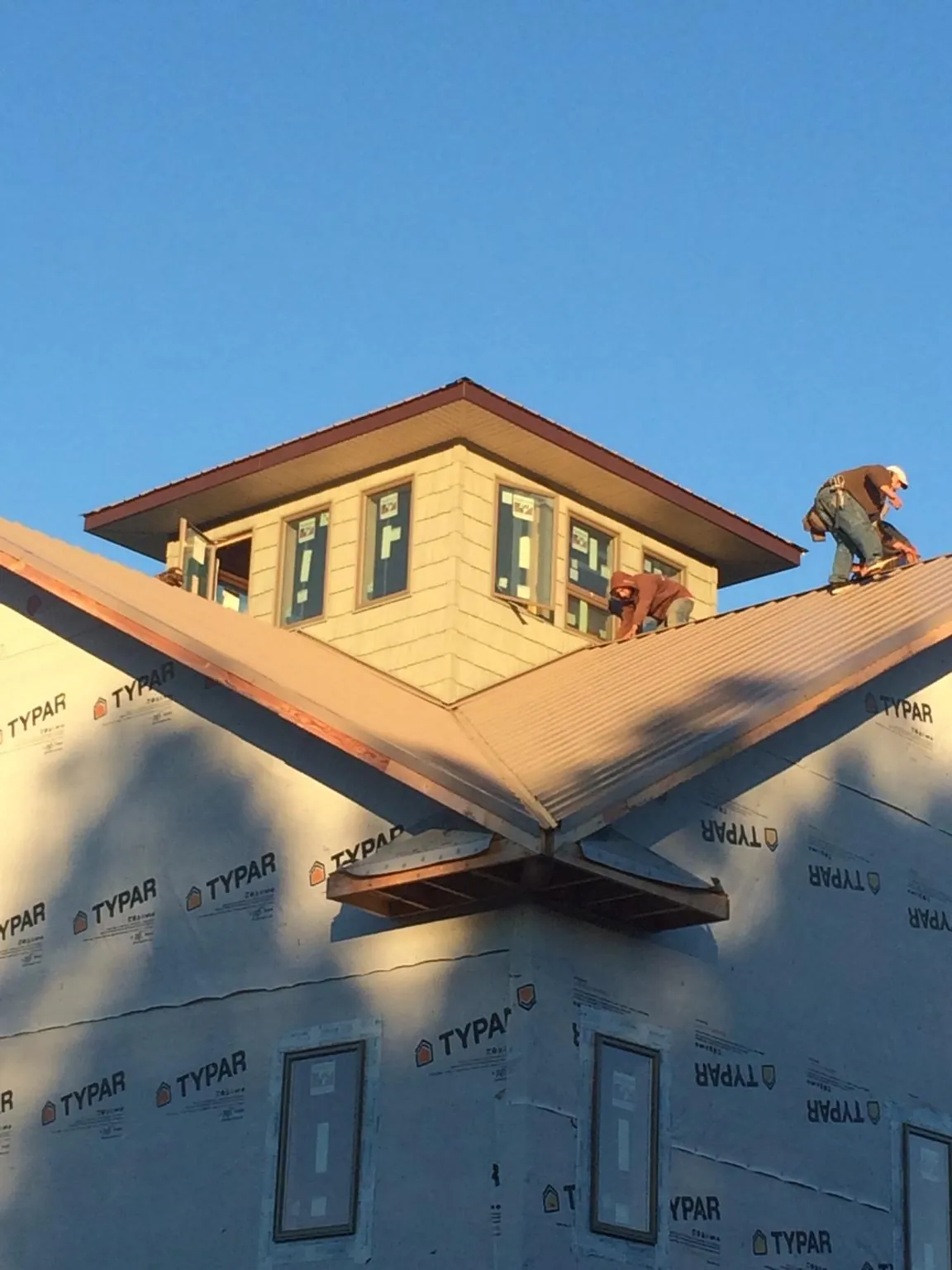 Roofers working around a rooftop cupola on a new metal roof at sunset in Keansburg